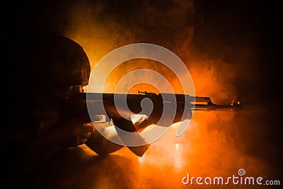 Silhouette of man with assault rifle ready to attack on dark toned foggy background or dangerous bandit holding gun in hand Stock Photo