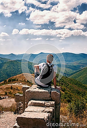 Silhouette of man with backpack sitting with his back to the photographer on the big rock and looking at the panorama of Editorial Stock Photo