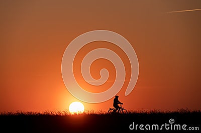 Silhouette of man on bike on grass on sunset with back lite and sun on backgound Stock Photo