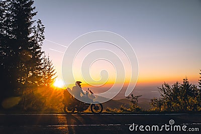 Silhouette of man biker and adventure motorcycle on the road with sunset light background. Top of mountains, tourism motorbike, Stock Photo