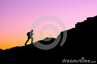 The silhouette of a man climbing a mountain in the sunset light Stock Photo