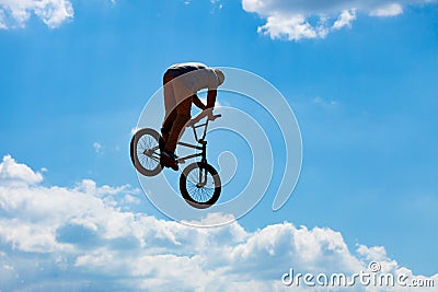 Silhouette of a man jumping on a Bicycle against a blue sky with white clouds. Stock Photo