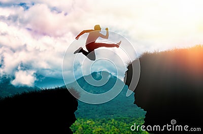 The silhouette of a man jumping over a chasm between rocks. In the background, the ocean and the sky. The concept of Stock Photo