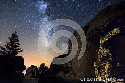 Silhouette of a man in the night exploring a cave in the mountain with a torch under an amazing the milky way Stock Photo