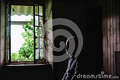 Silhouette of a man in an old uninhabitable house in front of a window. Depression, loneliness, despair, decline, sadness concept Stock Photo