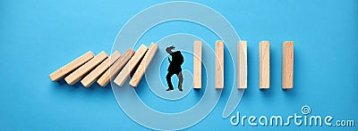 Silhouette of a man in panic try to protect himself against collapsing wooden dominos on blue background. Business crisis and Stock Photo