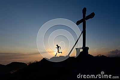 Silhouette of man running in the setting sun on top of a mountain with the cross Stock Photo