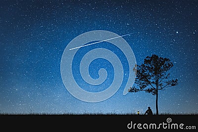 Silhouette of man sitting on mountain and night sky with shooting star. Alone concept Stock Photo