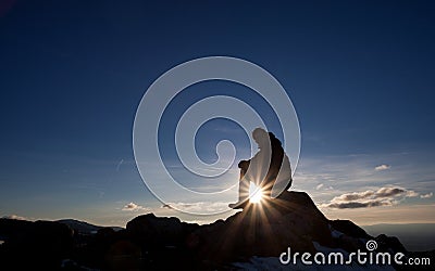 Silhouette of man sitting on peak in sunset Stock Photo