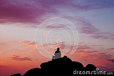 Silhouette of a man sitting on a rock during sunset. Stock Photo