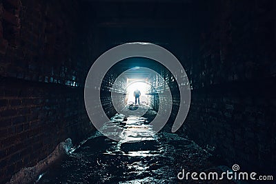 Silhouette of man standing in dark underground corridor. Light at end of tunnel concept Stock Photo