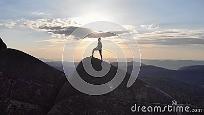 The silhouette of a man standing triumphantly on a mountain top at sunset. Stock Photo
