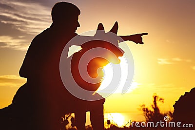 Silhouette of a man walking with a dog on the field at sunset, guy training pet in summer nature, boy giving a command Stock Photo