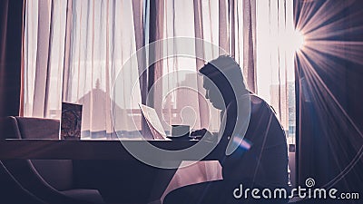 Silhouette of man at work using laptop against window background illuminated by natural sun glare Stock Photo