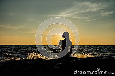 Silhouette meditation girl lotus position on stone on the background of the stunning sea. Stock Photo