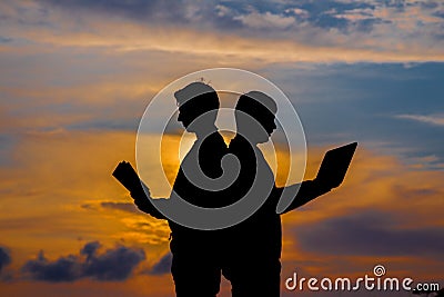 Silhouette of a men with laptop and a book on sunset or sunrise background. The idea of the contradictions of the old and new Stock Photo