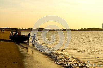 Silhouette of men pushing a tourist fishing boat into the ocean at a Gujarat beach Stock Photo