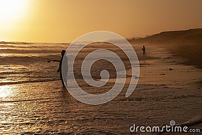 Silhouette of men surf fishing among ocean waves at sunset Editorial Stock Photo