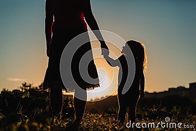 Silhouette of mother and daughter holding hands at sunset Stock Photo