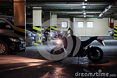 Silhouette of motorcycle standing with running engine in front of parked vehicles in underground parking area Stock Photo