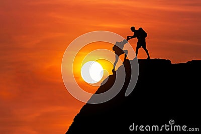 Silhouette mountaineer gives helping hand his friend to climb high cliff mountain together. Stock Photo