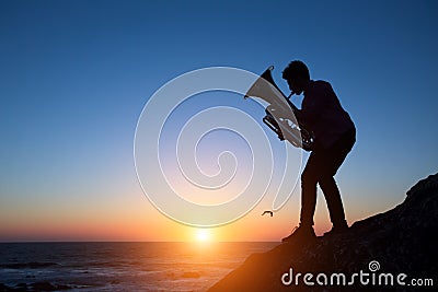 Silhouette of musician play Tuba on sea shore at amazing sunset .Art. Stock Photo