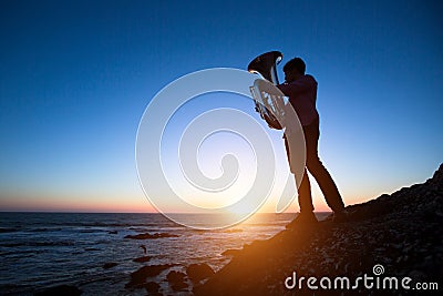 Silhouette of musician with Tuba on rocky sea coast Stock Photo