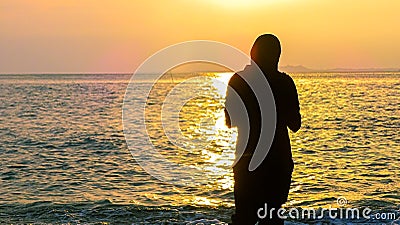 Silhouette muslim woman with hijab enjoying beautiful golden sunrise on the beach Stock Photo