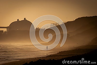 Silhouette of one person at San Onofre State beach at sunset with a nuclear power plant in the background Stock Photo
