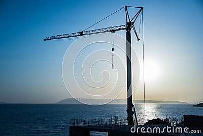 Silhouette, outline of the crane on the construction site against the blue sky and the sea. Details of the building, ribbed walls Stock Photo