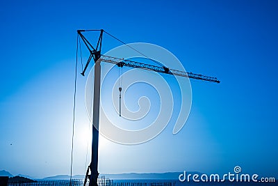 Silhouette, outline of the crane on the construction site against the blue sky and the sea. Details of the building, ribbed walls Stock Photo