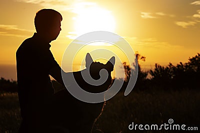 Silhouette profile of a young man and a dog watching the sun set on the horizon in a field, boy fondle his pet on nature, concept Stock Photo