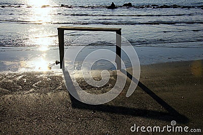 Silhouette of a simple wooden structure in the sea with its shadow on the shore and the reflection of the rays of the setting sun Stock Photo