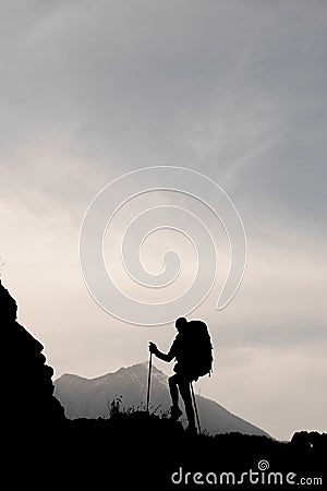 Silhouette slim girl standing on the rock with hiking backpack and walking sticks Stock Photo