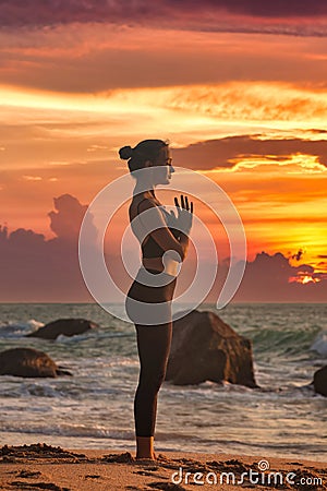 Silhouette slim woman does yoga on tropical sea coast or ocean beach outdoors at sunset Stock Photo