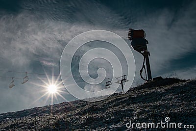 Silhouette of a snow cannon or artificial snow maker on a ski slope on a sunny day. Visible sun flare behind the exhaust of a Editorial Stock Photo