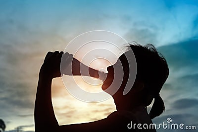 Silhouette of sport woman drinking water on sunset. Stock Photo