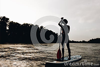 silhouette of sportswoman standing on paddleboard Stock Photo