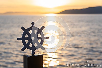 Silhouette of a stylized steering wheel of a ship on the dock, against the backdrop of a sunset. Space for text. Stock Photo