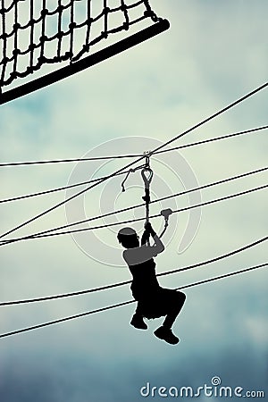 Silhouette of a teenage boy ziplining on zipline against cloudy sky background Stock Photo