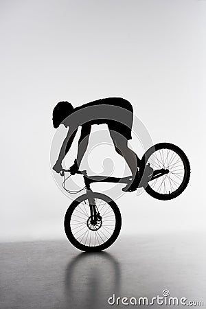 silhouette of trial biker performing front wheel stand Stock Photo