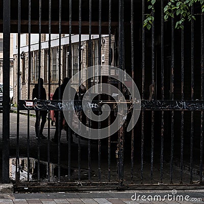 Silhouette of two persons meeting behind a locked barred gates Stock Photo