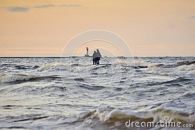 Silhouette of two unrecognizable persons standing on Mangalsala pier in wavy sea in sunset Stock Photo