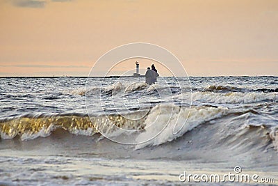 Silhouette of two unrecognizable persons standing on Mangalsala pier in wavy sea in sunset Stock Photo