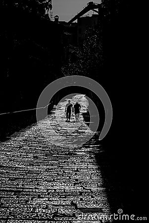 Silhouette of two walking people by the street of paving stones, in black and white colors. Stock Photo