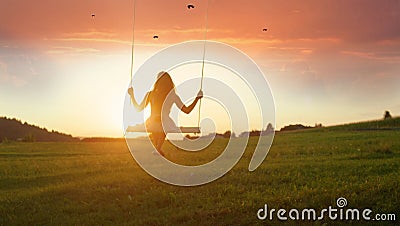 SILHOUETTE: Unknown girl swaying on wooden swing at golden sunset in spring Stock Photo