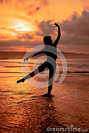 silhouette of a very slender ballerina doing ballet practice alone on the seashore with waves crashing at her Stock Photo