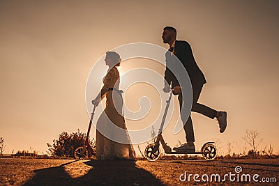 Silhouette wedding couple riding a on scooters along the road outside the city at sunset. Stock Photo