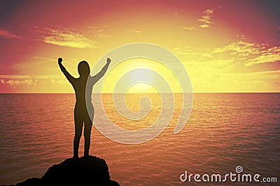 Silhouette of winning success woman at sunset or sunrise standing and raising up hand in celebration of having reached mountain. Stock Photo