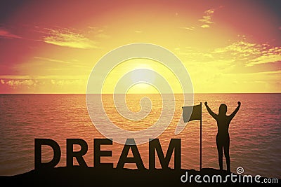 Silhouette of winning success woman at sunset or sunrise standing and raising up hand near flag with text DREAM Stock Photo